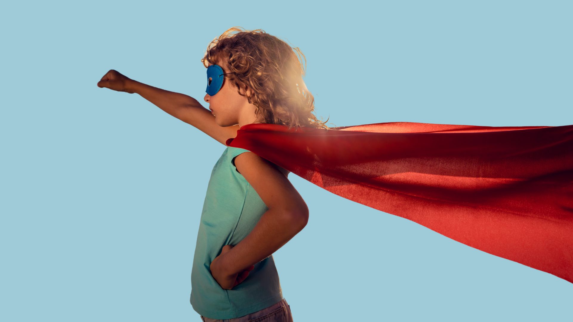 Eit barn med ei kappe som strekkjer armen mot himmelen som ein superhelt.