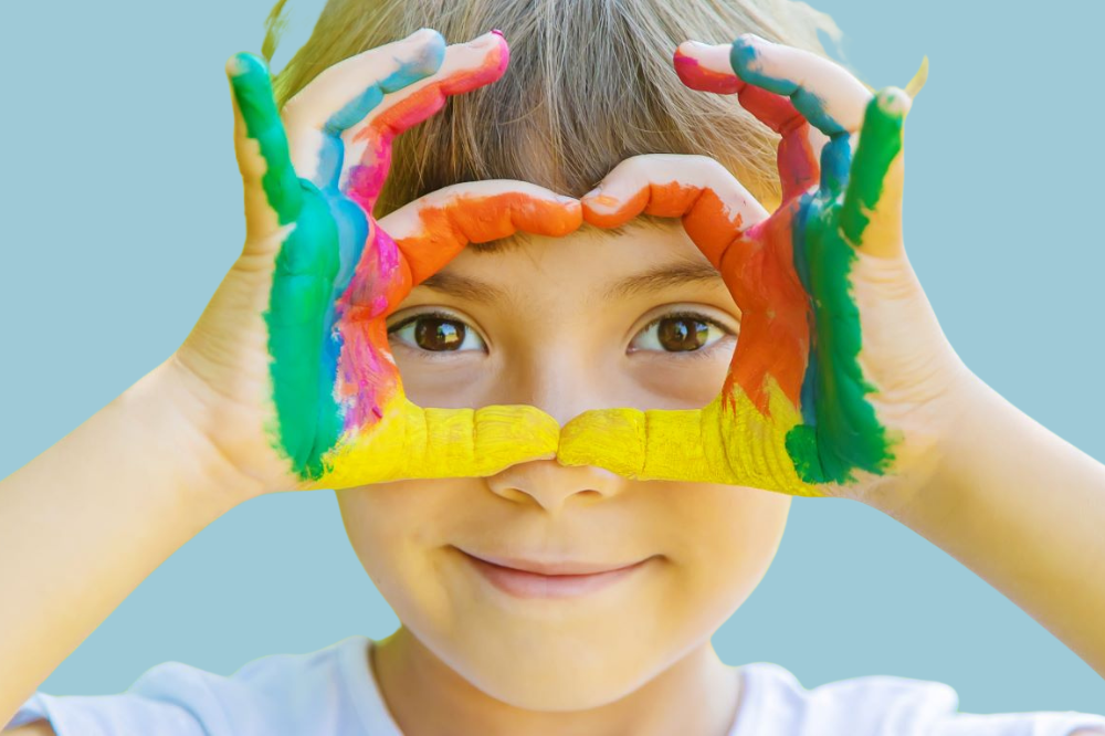 Ei jente med måla hender lagar ein figur framfor auga.