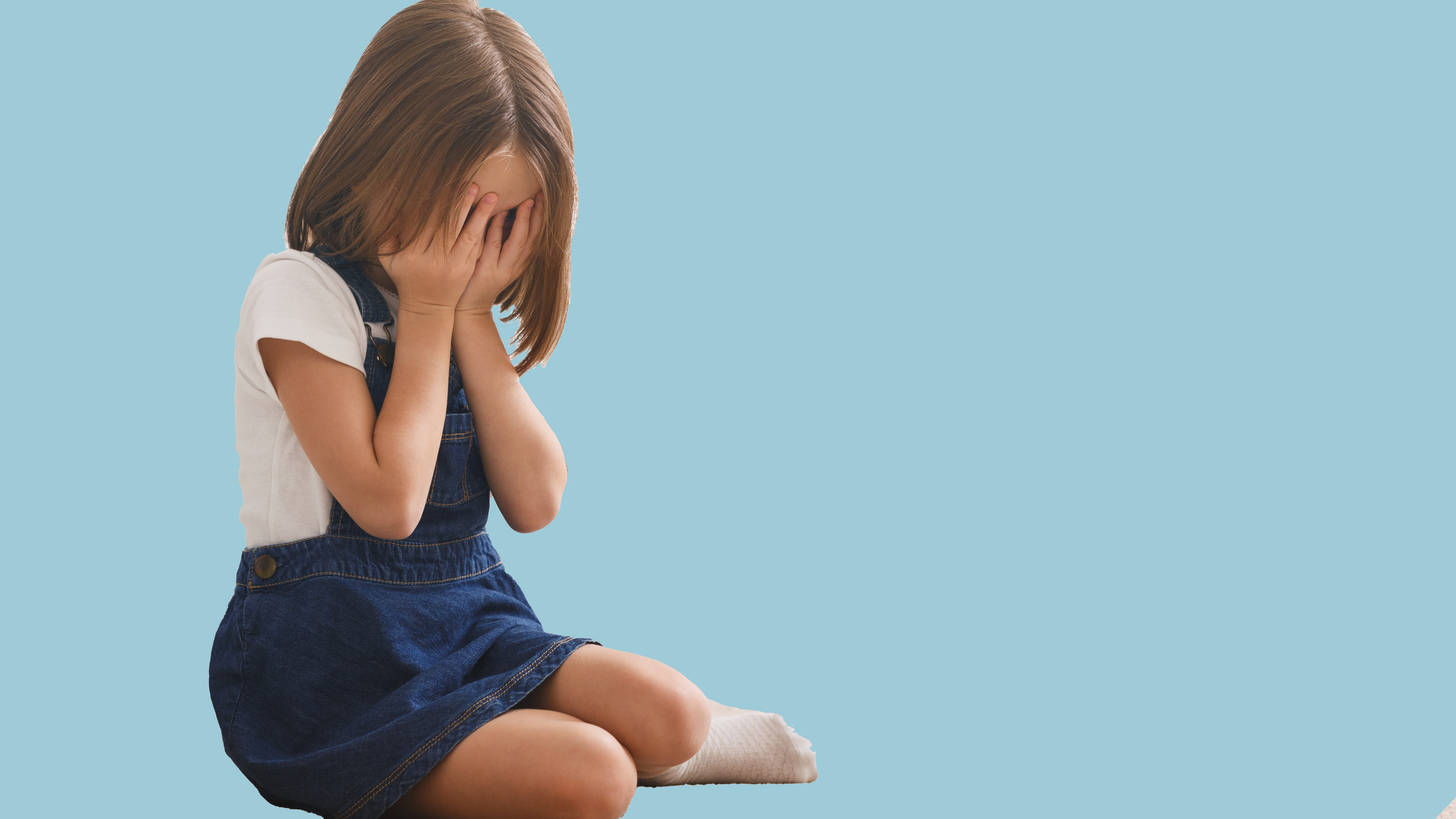 Gråtande lita jente med auga dekka som sit på golvet.