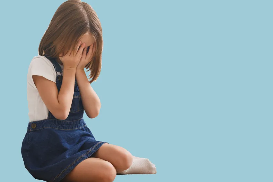 Gråtande lita jente med auga dekka som sit på golvet.