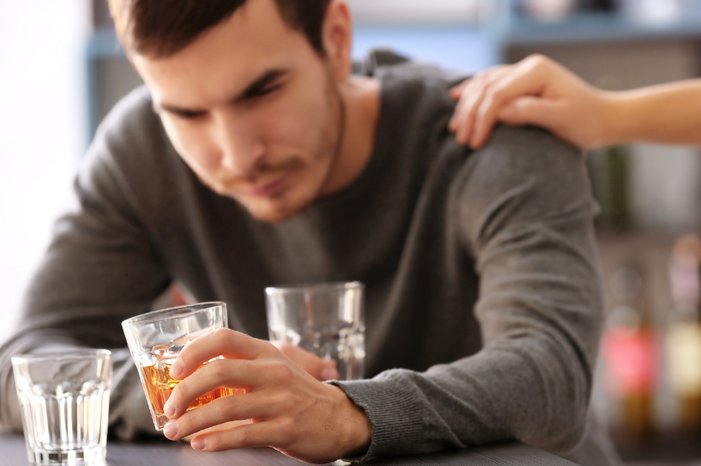 Ein mann som held eit glas med brennevin. Ei hand held han på skuldra.