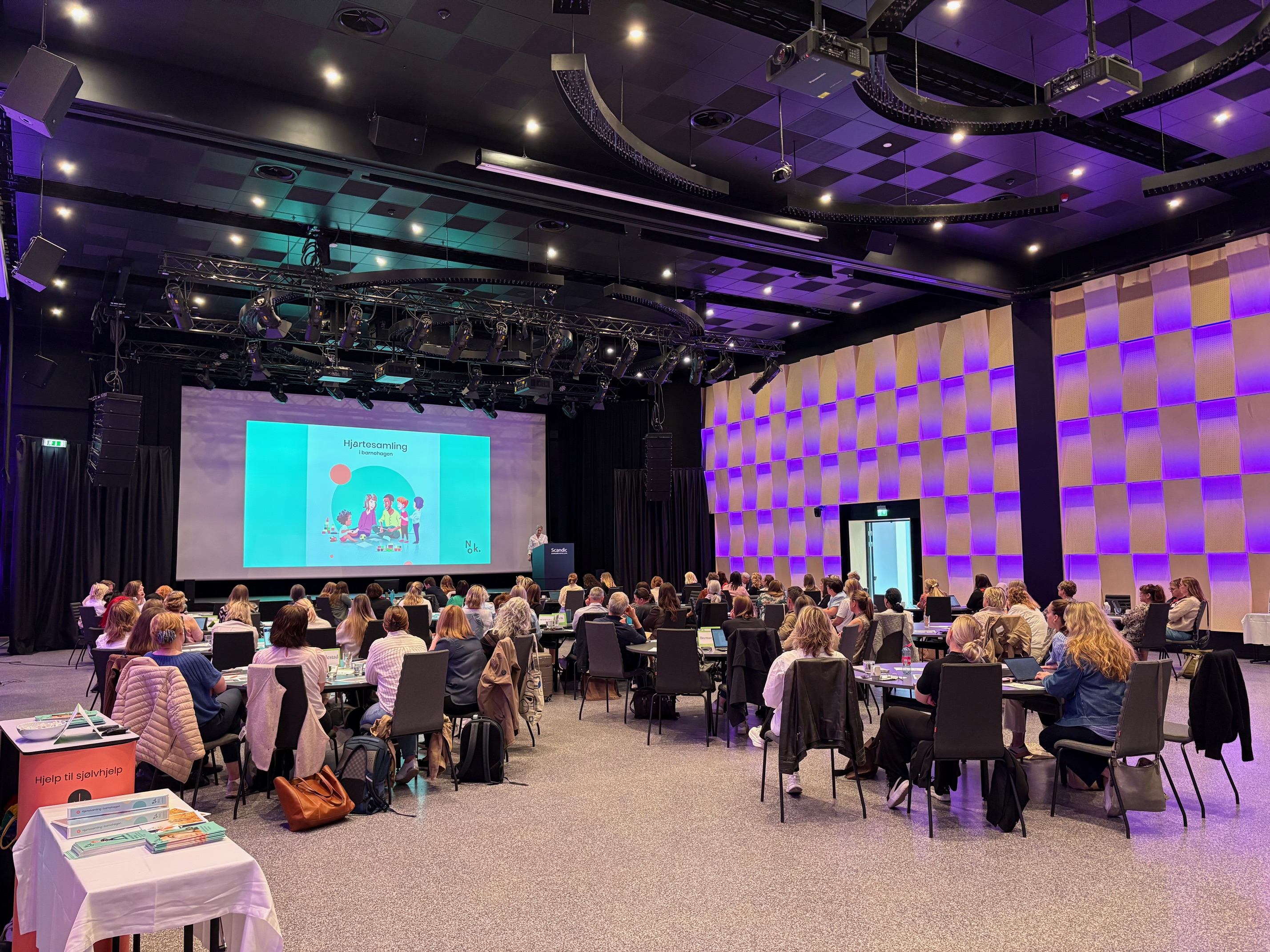 Ei gruppe menneske som sit i eit rom med ein stor skjerm