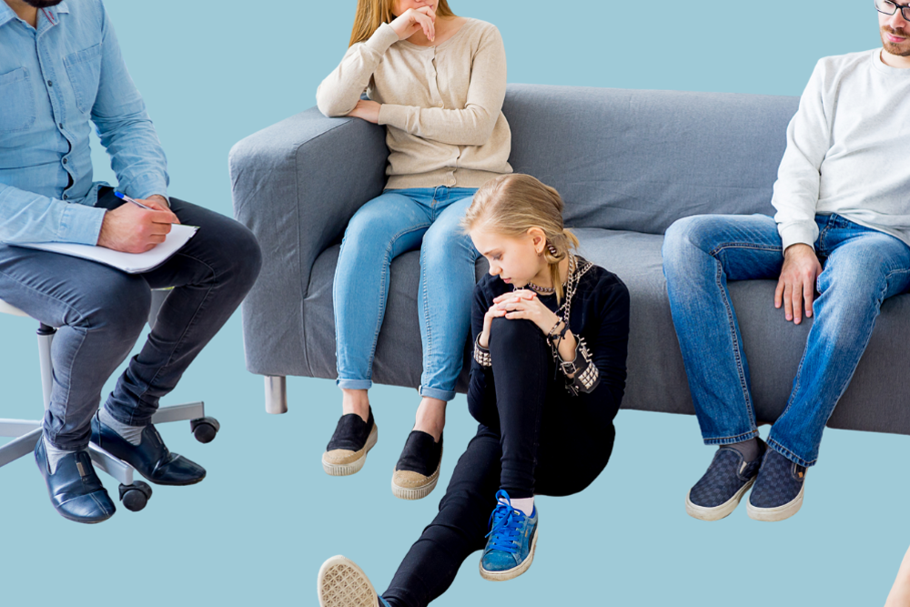 Fleire personar som sit i eit rom, med fokus på ei jente som sit på golvet.